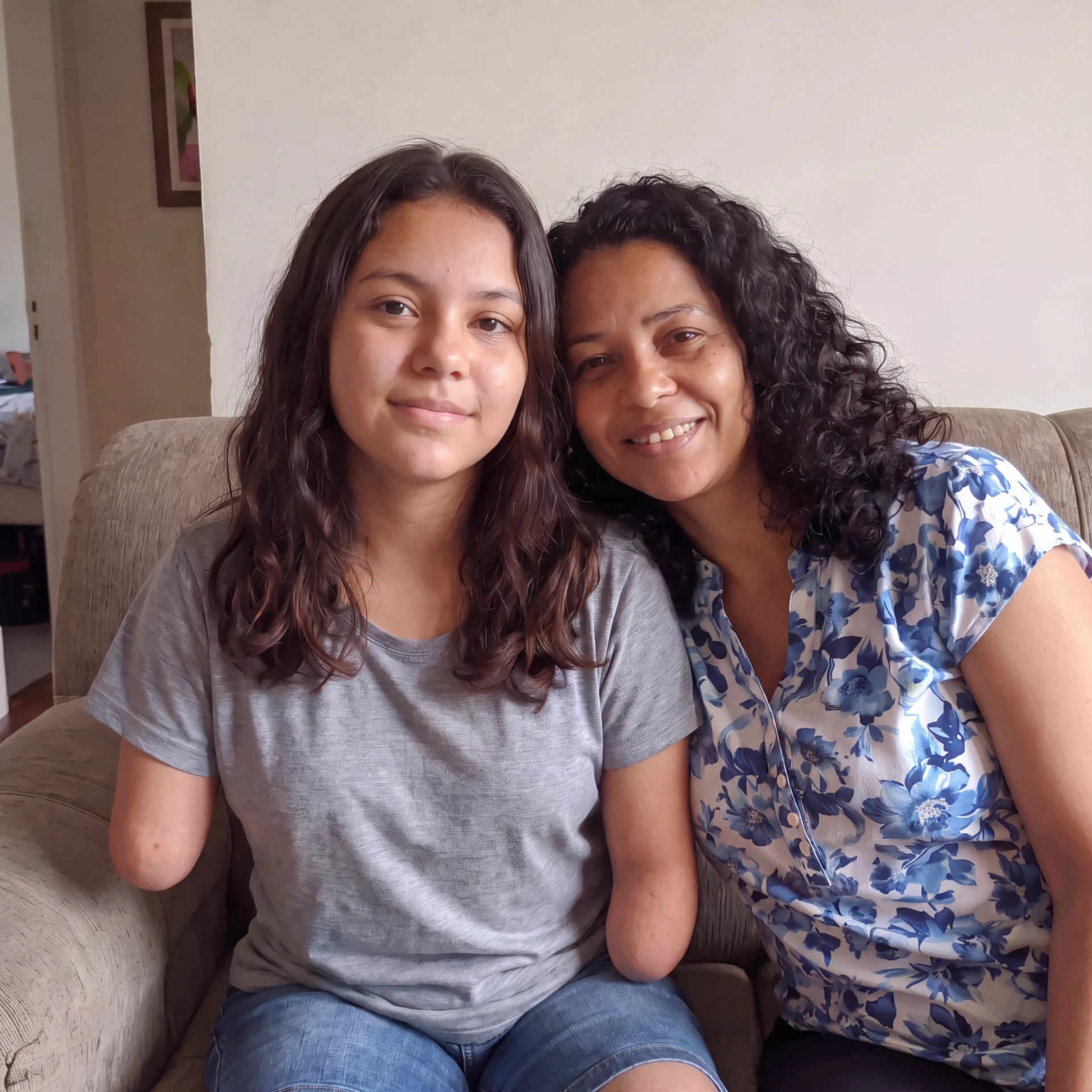 Rebeca e a mãe, sentadas juntas no sofá de casa